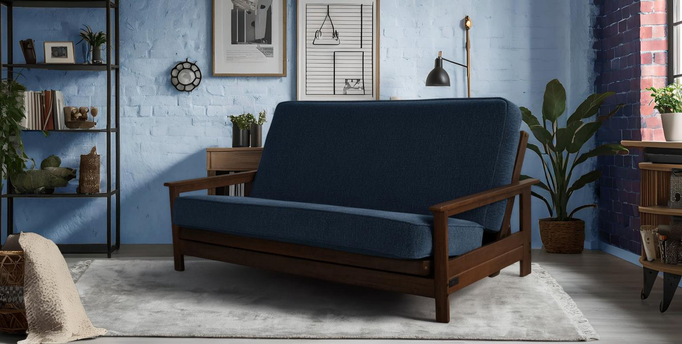 Blue futon sofa in a room with blue brick walls, shelves, and plants.