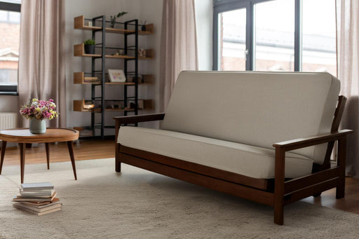 Beige futon sofa in a room with a bookshelf and coffee table.