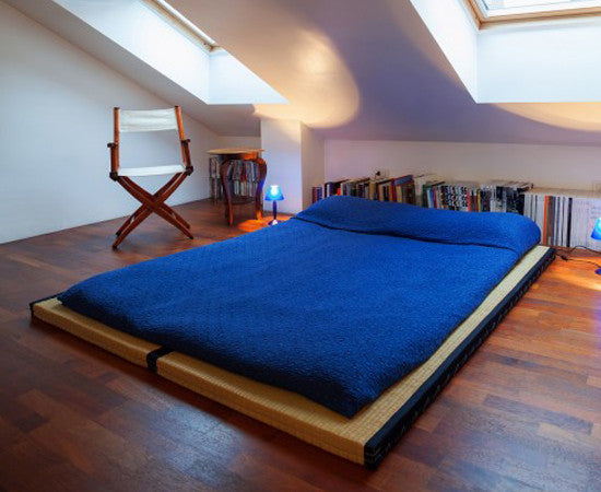 Two Tatami Mats in loft bedroom under skylights with shikibuton futon mattress on top of them with a folding side chair to the side and books lining the wall